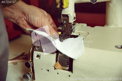 Image of Sewing process of the leather belt. old Man\'s hands behind sewing.