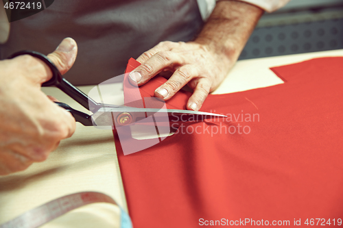 Image of Closeup of tailors table with male hands tracing fabric making pattern for clothes