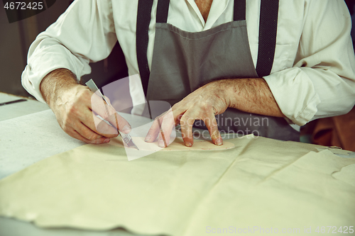 Image of Closeup of tailors table with male hands tracing fabric making pattern for clothes