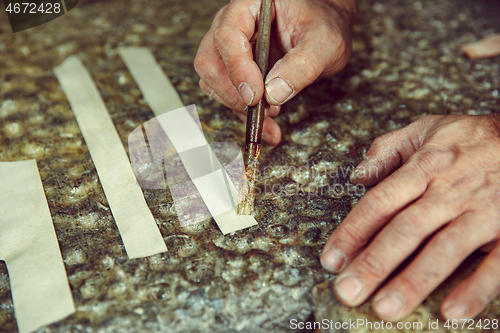 Image of Shoemaker makes shoes for men.He smears special liquid with a brush.