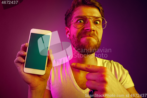 Image of Indoor portrait of attractive young man holding blank smartphone