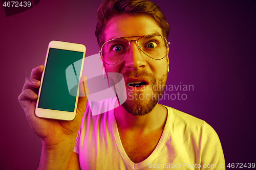 Image of Indoor portrait of attractive young man holding blank smartphone