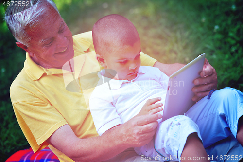 Image of grandfather and child in park using tablet