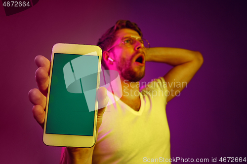 Image of Indoor portrait of attractive young man holding blank smartphone