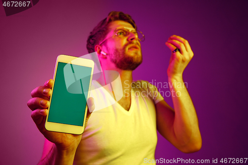 Image of Indoor portrait of attractive young man holding blank smartphone