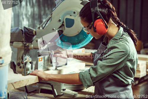 Image of Busy and serious craftswoman grinding timbers with special machine.