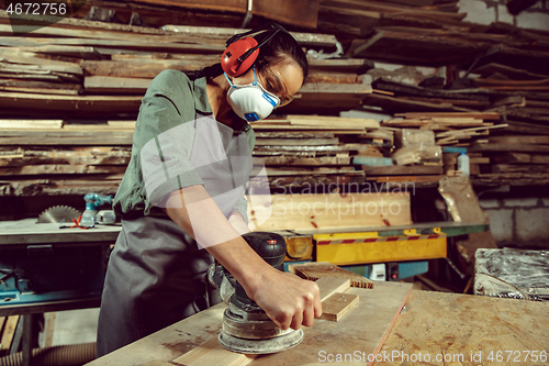 Image of Busy and serious craftswoman grinding timbers with special machine.