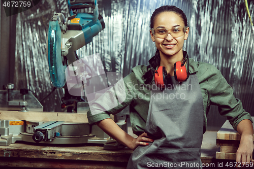 Image of Smiling craftswoman grinding timbers with special machine.