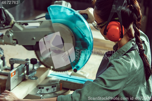 Image of Busy and serious craftswoman grinding timbers with special machine.