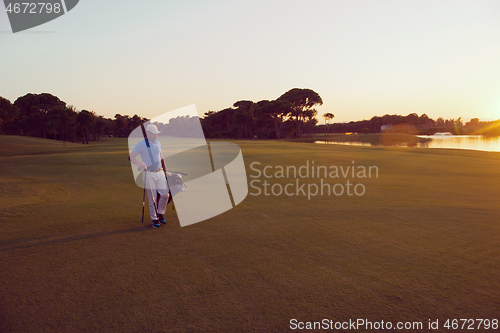 Image of golfer  walking and carrying golf  bag at beautiful sunset