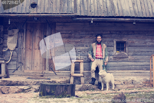 Image of hipster with dog in front of wooden house