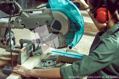 Image of Busy and serious craftswoman grinding timbers with special machine.