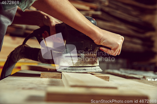 Image of Hands of craftswoman grinding timbers with special machine.