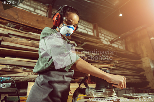 Image of Busy and serious craftswoman grinding timbers with special machine.