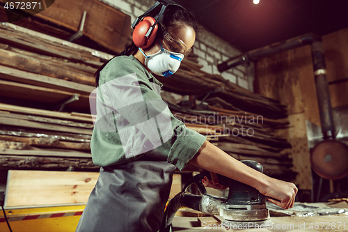 Image of Busy and serious craftswoman grinding timbers with special machine.