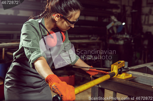 Image of Busy and serious craftswoman grinding timbers with special machine.