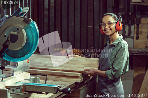 Image of Smiling craftswoman grinding timbers with special machine.