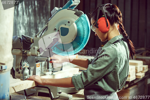 Image of Busy and serious craftswoman grinding timbers with special machine.