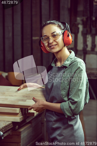 Image of Smiling craftswoman grinding timbers with special machine.