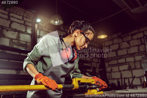 Image of Busy and serious craftswoman grinding timbers with special machine.