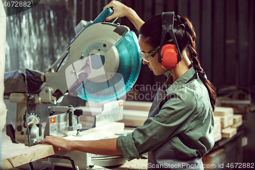 Image of Busy and serious craftswoman grinding timbers with special machine.