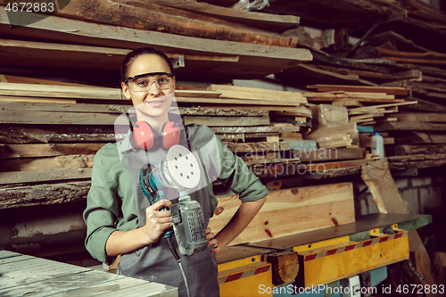 Image of Smiling craftswoman grinding timbers with special machine.