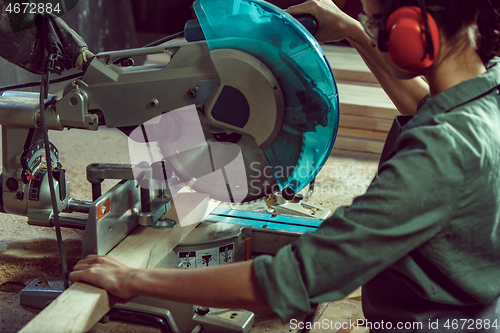 Image of Busy and serious craftswoman grinding timbers with special machine.