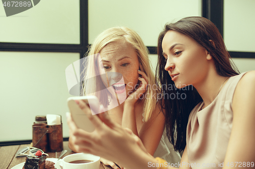 Image of Two girl friends spend time together drinking coffee in the cafe, having breakfast and dessert.