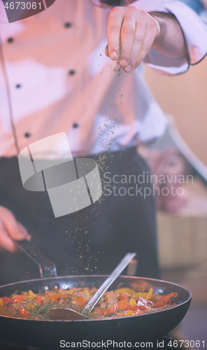 Image of chef putting spices on vegetables in wok