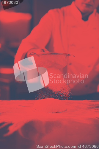 Image of chef sprinkling flour over fresh pizza dough