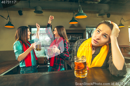 Image of Sport, people, leisure, friendship and entertainment concept - happy football fans or female friends drinking beer and celebrating victory at bar or pub