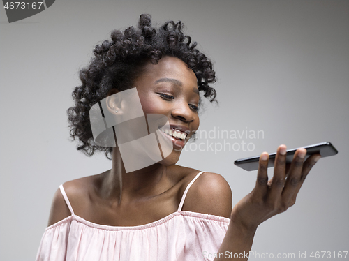 Image of Indoor portrait of attractive young black woman holding blank smartphone