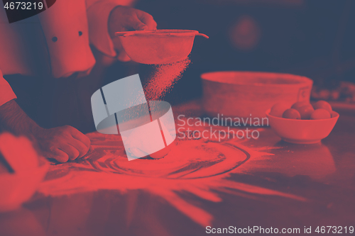 Image of chef sprinkling flour over fresh pizza dough