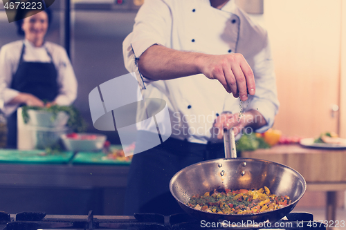 Image of chef putting spices on vegetables in wok