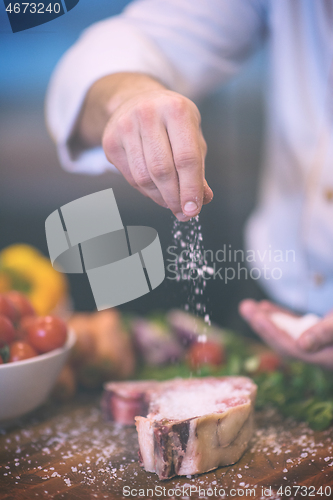 Image of Chef putting salt on juicy slice of raw steak