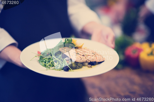 Image of Chef hands holding dish of fried Salmon fish fillet