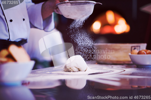 Image of chef sprinkling flour over fresh pizza dough