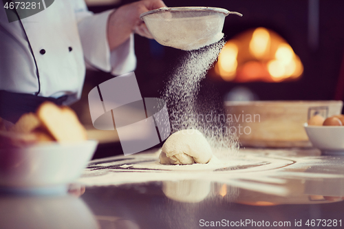 Image of chef sprinkling flour over fresh pizza dough