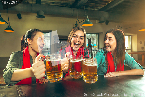 Image of Sport, people, leisure, friendship and entertainment concept - happy football fans or female friends drinking beer and celebrating victory at bar or pub