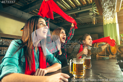 Image of Sport, people, leisure, friendship and entertainment concept - happy football fans or female friends drinking beer and celebrating victory at bar or pub