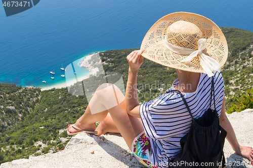 Image of Active sporty woman on summer vacations sitting on old stone wall at Lubenice village, wearing straw hat and beach backpack enjoying beautiful coastal view of Cres island, Croatia