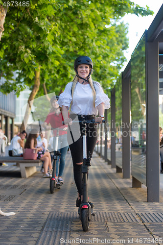 Image of Trendy fashinable teenager girls riding public rental electric scooters in urban city environment. New eco-friendly modern public city transport in Ljubljana, Slovenia