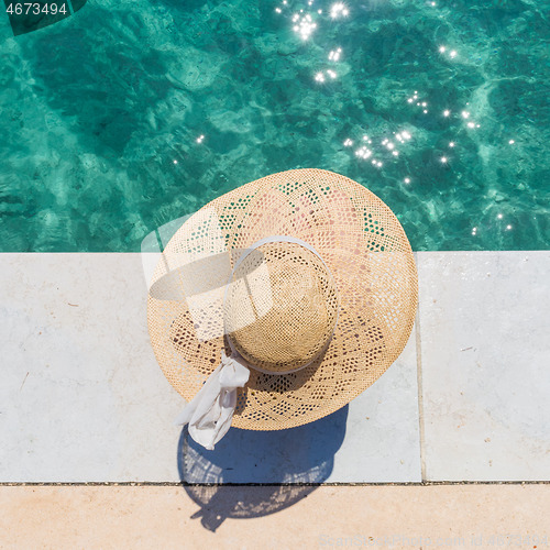 Image of Woman wearing big summer sun hat relaxing on pier by clear turquoise sea.