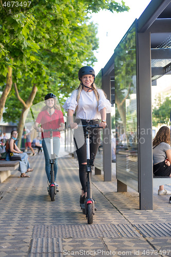 Image of Trendy fashinable teenager girls riding public rental electric scooters in urban city environment. Eco-friendly modern public city transport