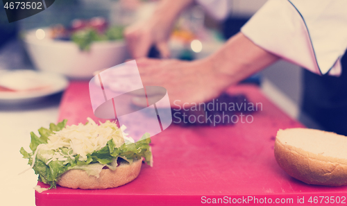 Image of chef hands cutting salad for burger