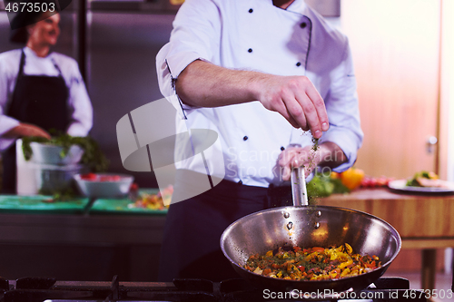 Image of chef putting spices on vegetables in wok