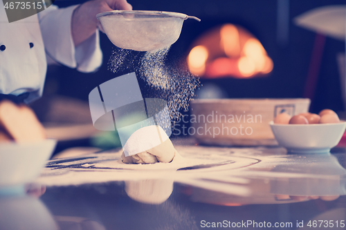 Image of chef sprinkling flour over fresh pizza dough