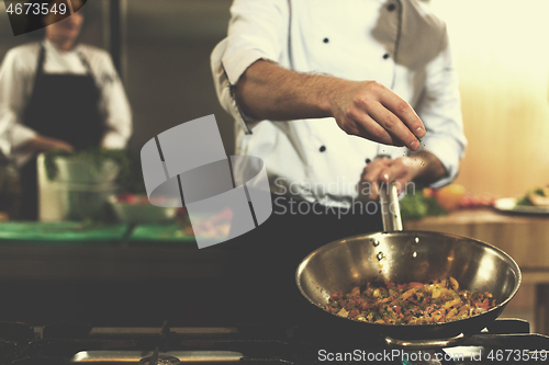 Image of chef putting spices on vegetables in wok