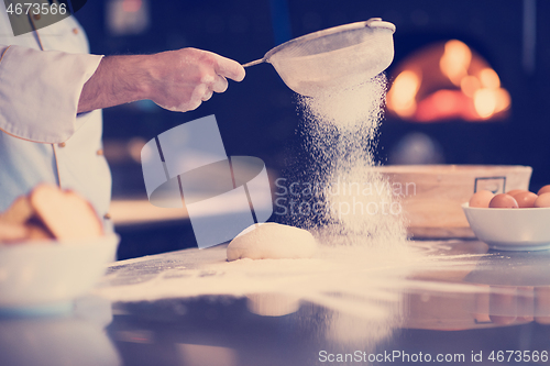 Image of chef sprinkling flour over fresh pizza dough