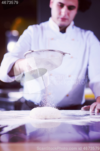 Image of chef sprinkling flour over fresh pizza dough